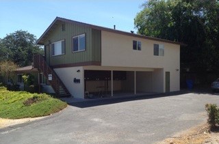 The same two-story building restored, with fresh green and cream siding and a clean, open carport.